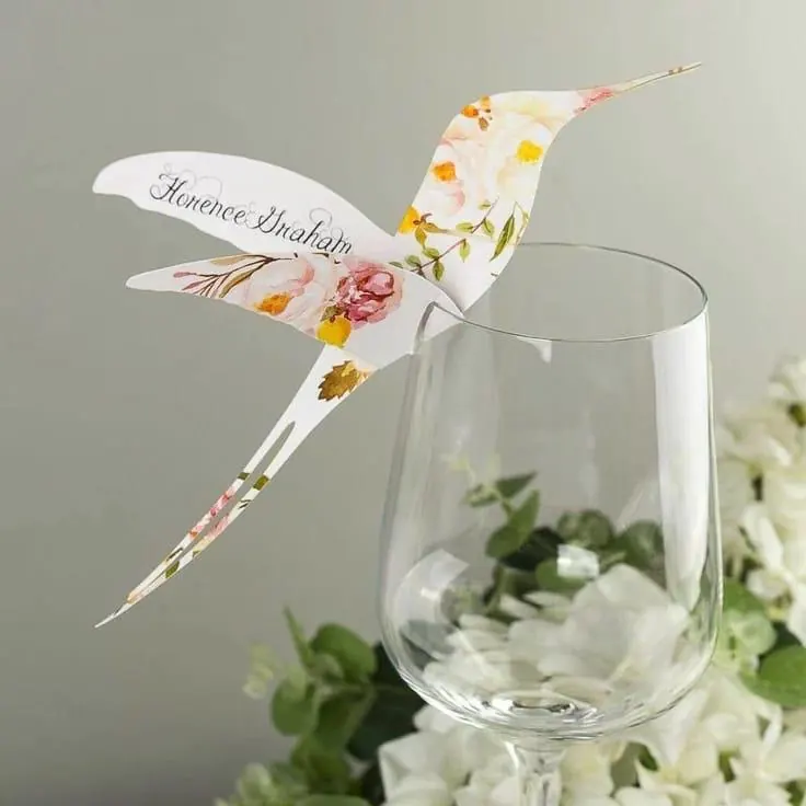 Die-cut floral hummingbird place card with guest name perched on a wine glass by StationeryWalaa